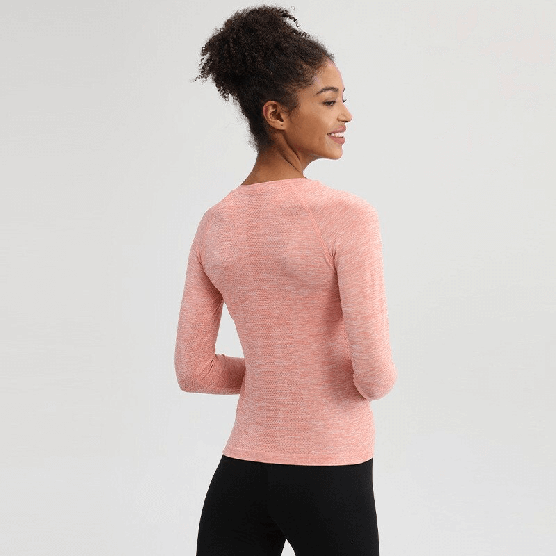 Woman wearing a pink solid color round neck yoga shirt with long sleeves and thumbs, ideal for fitness and comfort.